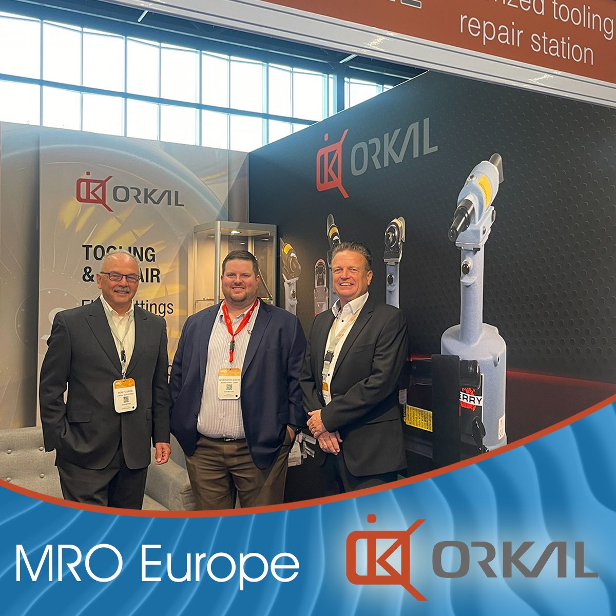 three men in business attire standing in front of an exhibit with the logo "orkal" at the mro europe 2023 event on day one.