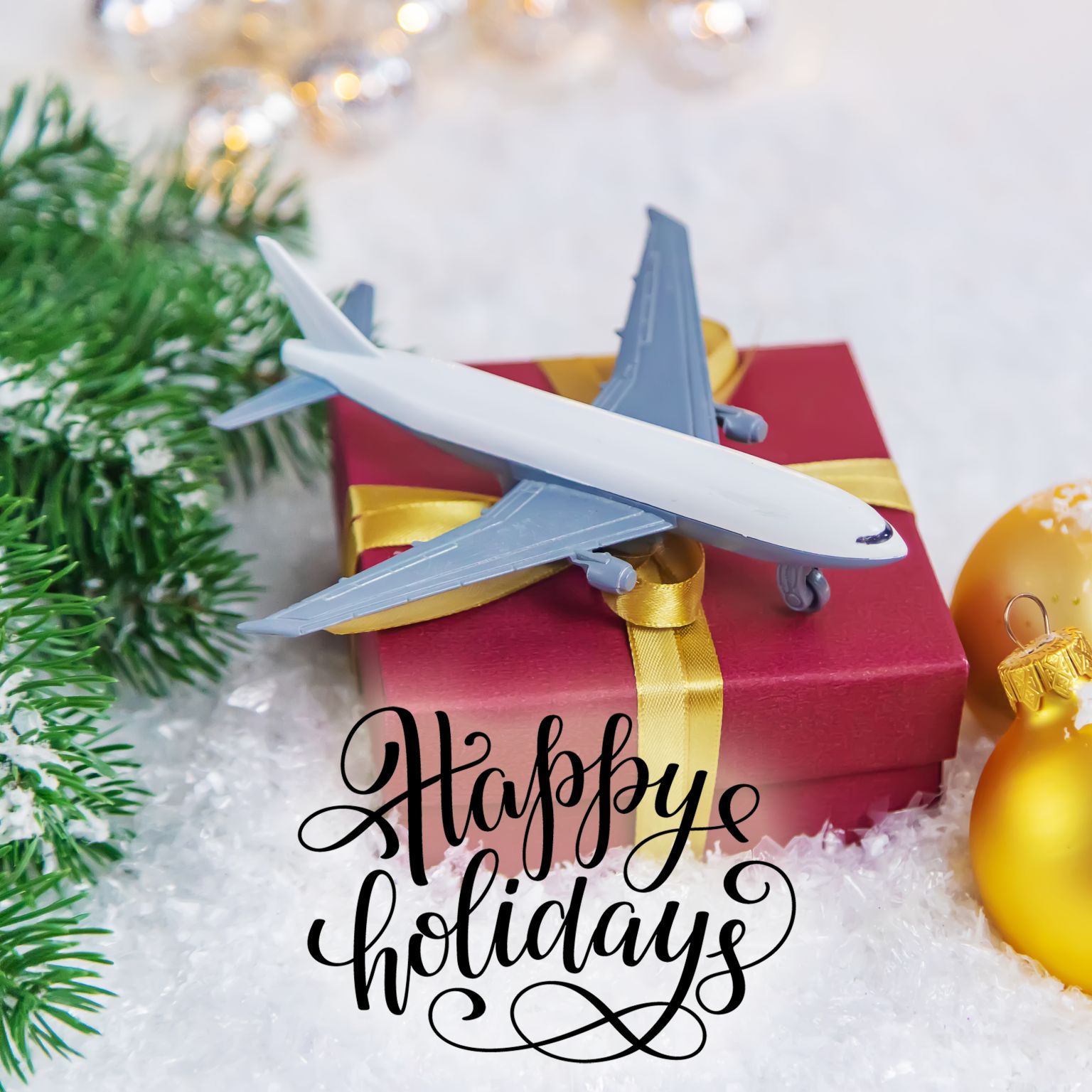 a toy airplane on a red gift box with a gold ribbon, accompanied by christmas ornaments and the text "happy holidays 2023.