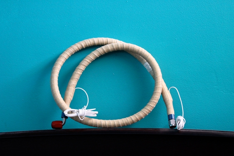a coiled beige aerospace hose with attached earbuds lying on a dark surface against a teal background.