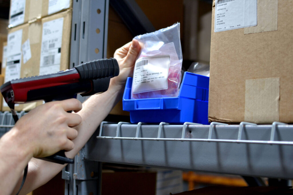 a worker scans a barcode on a packaged item in a warehouse using a handheld tooling scanner.