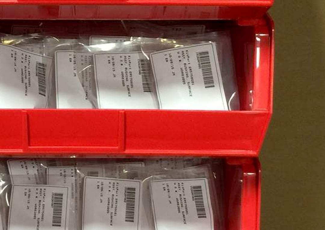 red bin containing multiple transparent packets with barcoded labels, placed for organized kitting solutions.